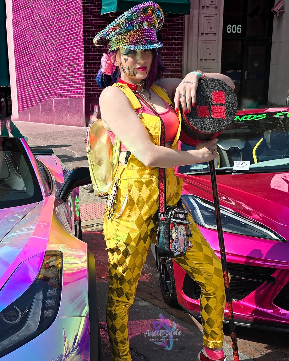 Ariel Jade in a gold harlequin costume between two sports cars