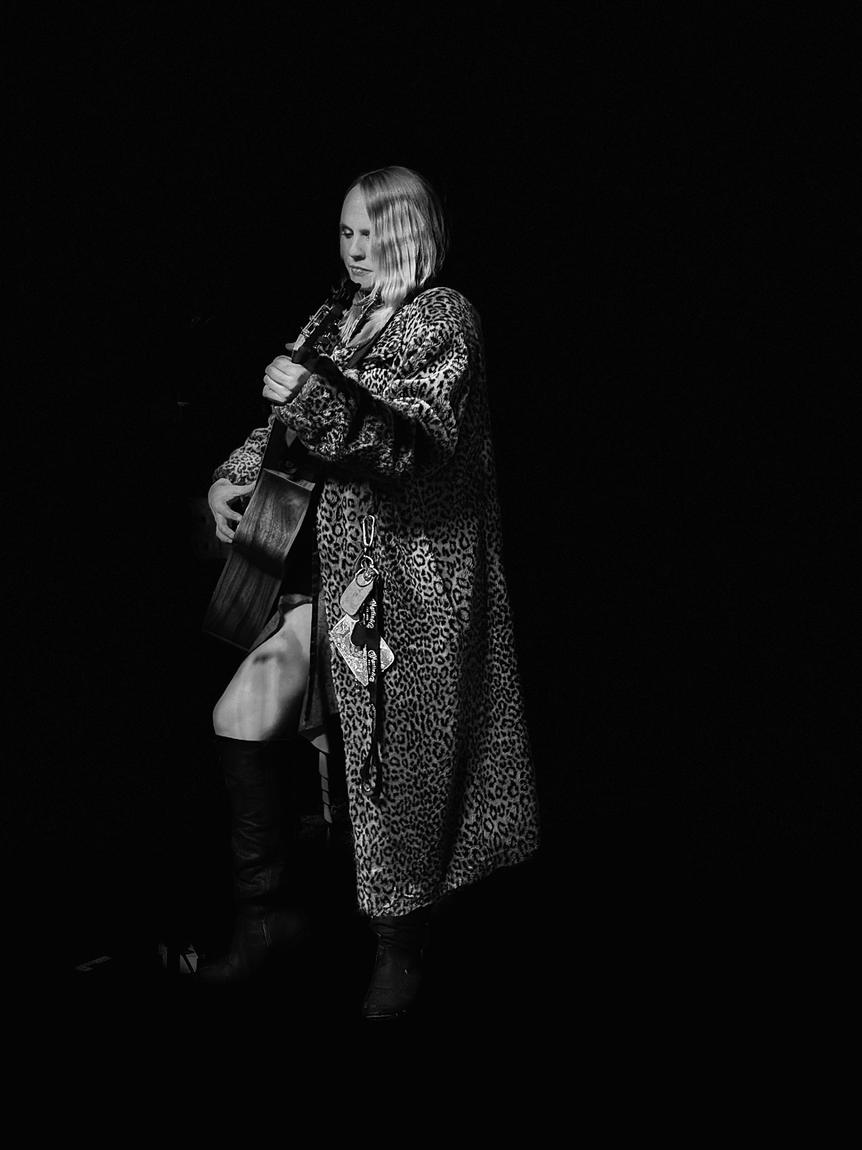 Black and white photo of Ariel Jade in a leopard coat with guitar