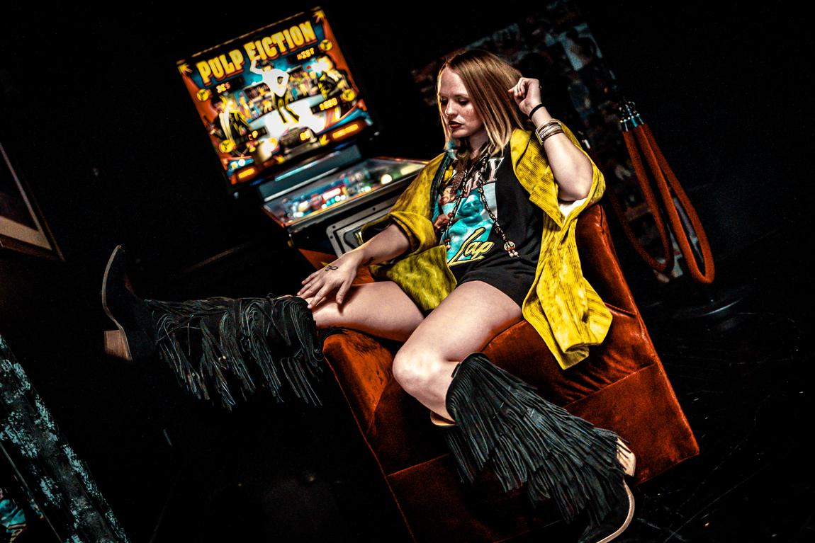 Ariel Jade in fringe boots beside a pinball machine